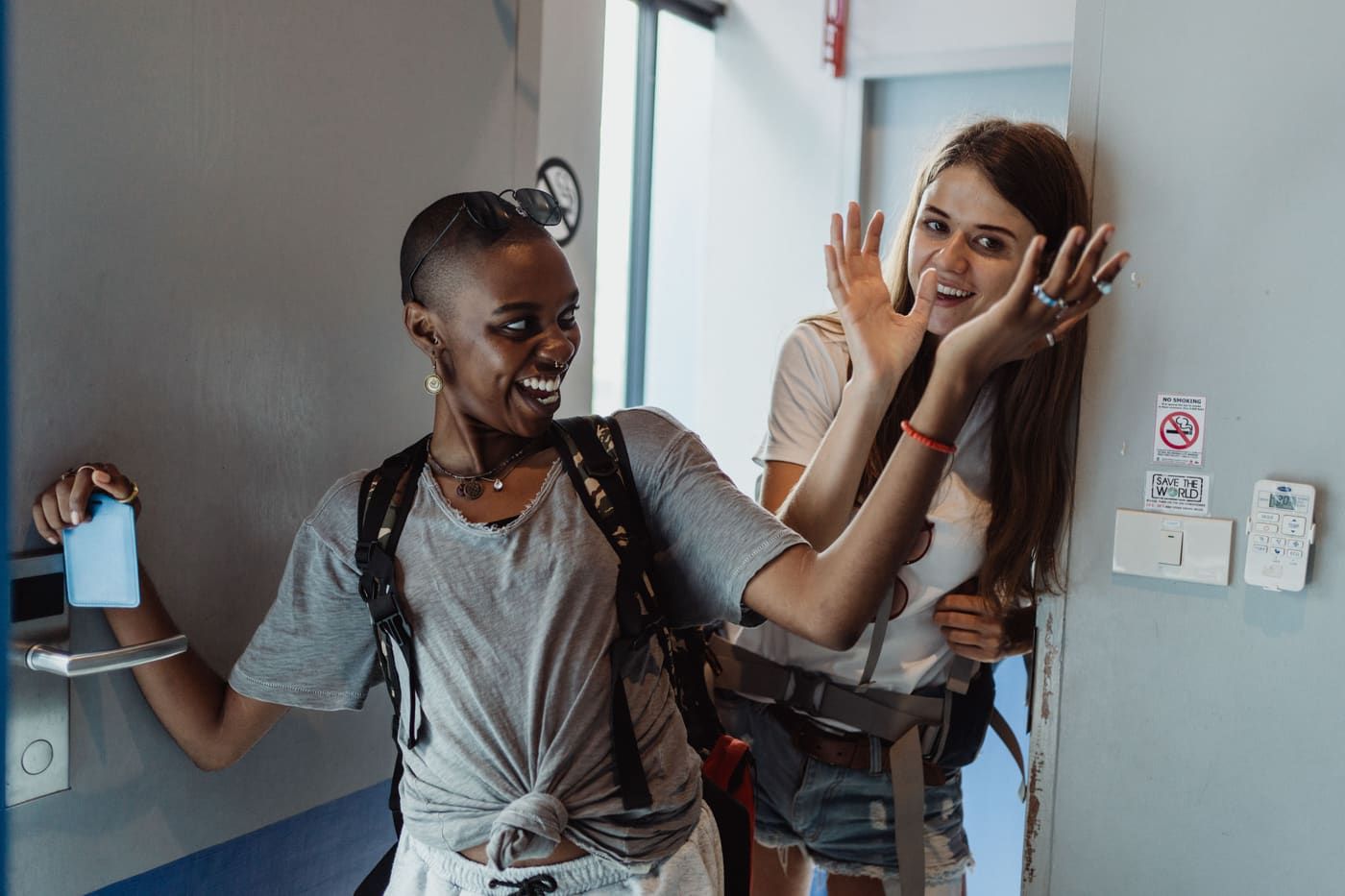 Two female travelers joyfully enter a hostel room, ready for adventure.
